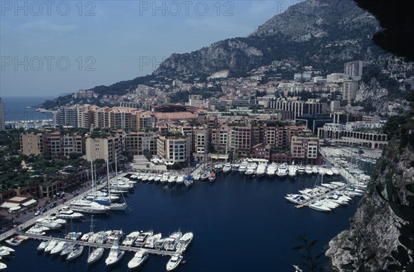MONACO, Fontvielle, Elevated view over harbour with moored yachts on water towards tall buildings and houses built into hillside