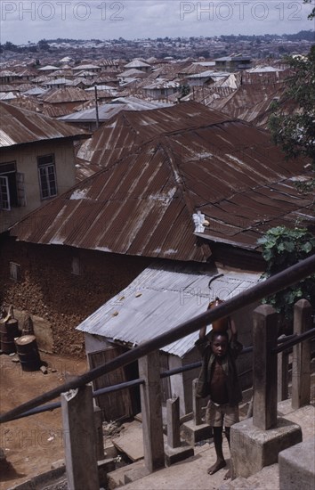 NIGERIA, Ibadan, View across corrugated tin rooftops of city houses with child carrying water jar in the foreground.
