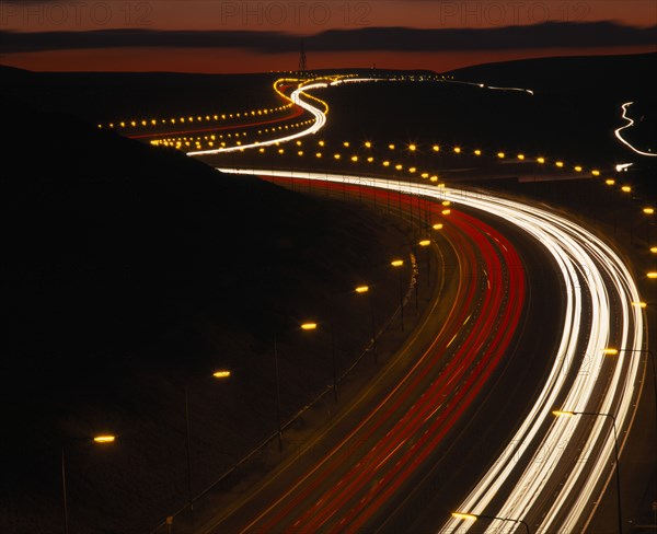 TRANSPORT, Traffic, Motorway, M62 Motorway. Elevated view over traffic in motion blur with light trails seen in late evening with a red sky