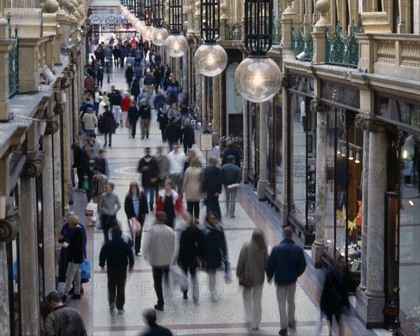 ENGLAND, Yorkshire, Leeds, Leeds County Arcade interior with shoppers walking along marbled walkway between pillar fronted shop fronts with glass globe shaped lighting above.