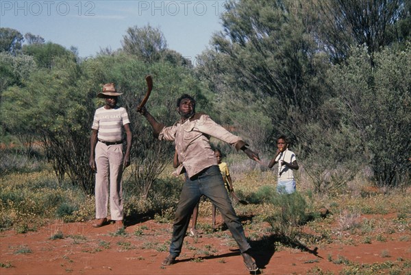 AUSTRALIA, Northern Territory, Alice Springs, Aborigine man throwing a Boomerang with a man and children standing behind him looking on