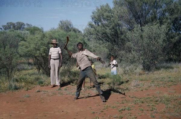 AUSTRALIA, Northern Territory, Alice Springs, Aborigine man throwing a Boomerang with a man and children standing behind him looking on