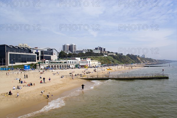 ENGLAND, Dorset, Bournemouth, The East Beach showing the Imax Complex and seafront attractions with people on the beach and at the waters edge between the groynes. Clifftop hotels and flats in the distance