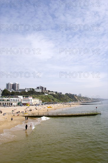 ENGLAND, Dorset, Bournemouth, The East Beach showing the seafront attractions with people on the beach and at the waters edge between the groynes. Clifftop hotels and flats in the distance
