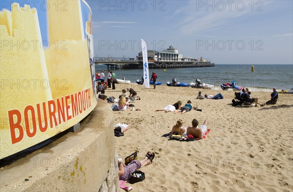 ENGLAND, Dorset, Bournemouth, People lying on the beach on a sunny day with Bournemouth Pier in the background