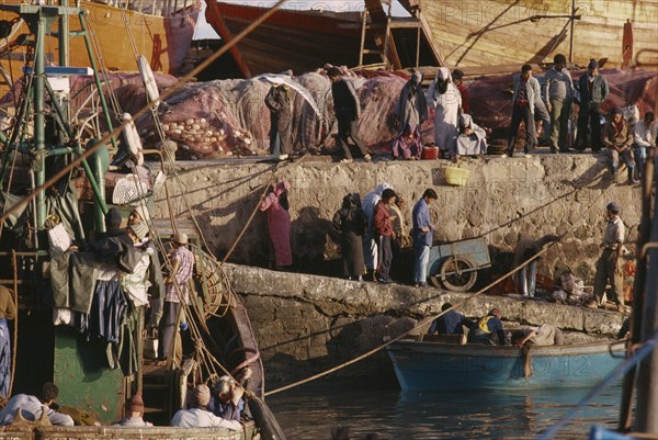 20077622 MOROCCO  Essaouira Busy port scene with moored fishing boat and crowds on stone quay.