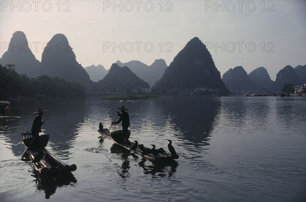 CHINA, Guangxi Province, River Li, Cormorant fishermen on stretch of river in the Guilin area with limestone peaks behind.