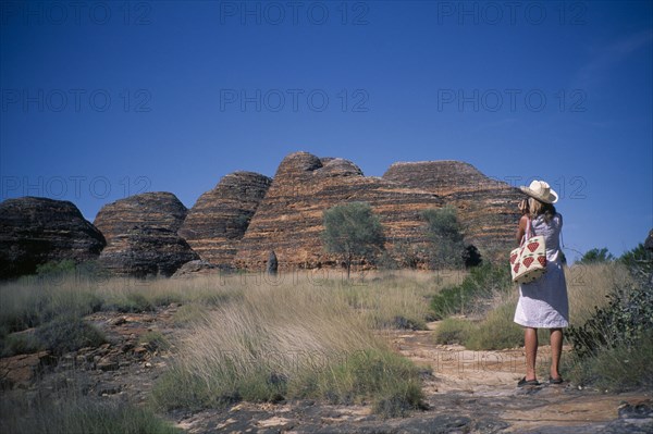 AUSTRALIA, Western ,  Kimberley, Purnululu or Bungle Bungle. Woman wearing straw hat taking picture of striped rock towers