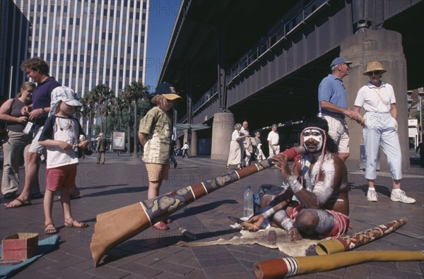 AUSTRALIA, New South Wales, Sydney, Circular Quay. Aboriginal Digeridoo player busking with people looking on