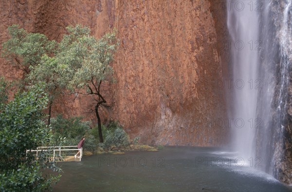 AUSTRALIA, Northern, Uluru, Ayers Rock. Maggie Springs. A woman viewing the cascading waterfall after torrential rainfall of 69mm in forty eight hours. An event that only happens once in every four years.