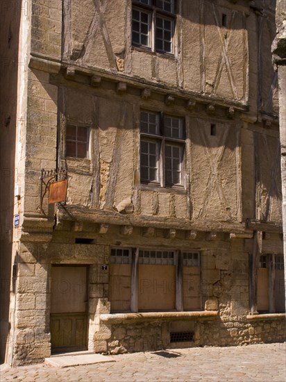 FRANCE, Deux Sevres Region, Poitiers, Very old wooden structured buiding in the town of Lusignan. Rusty sign hangs above the boarded up door.