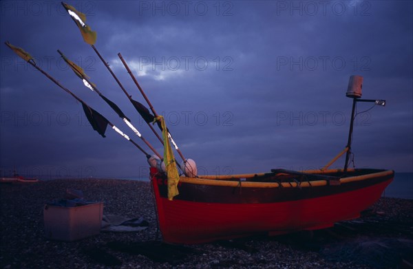 ENGLAND, West Sussex, Worthing, Red and yellow wooden fishing boat pulled up on shingle beach in evening light.