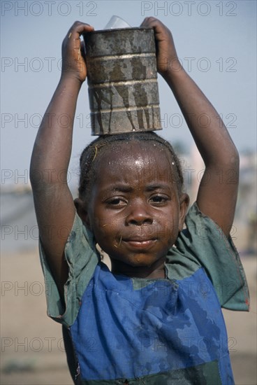 GUINEA, Kissidougou Camp, Little girl with braided hair at camp for refugees from Sierra Leone carrying can of water on her head.