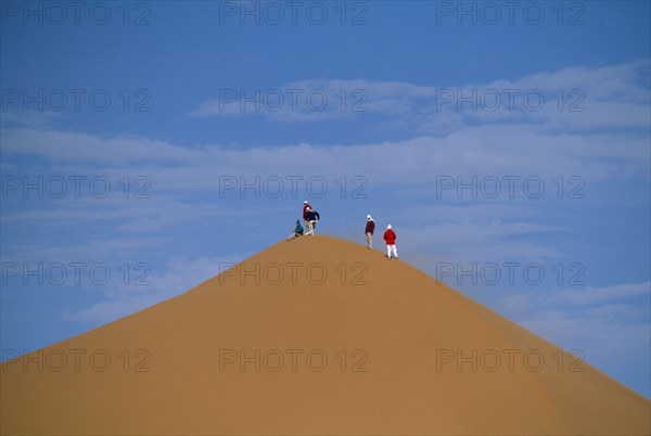 LIBYA, Sahara Desert, Tourists standing on top of Saharan sand dune.