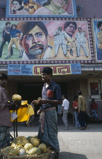 BANGLADESH, Dhaka, Cinema with colourful poster hoadings above entrance and men at a fruit stall in the foreground