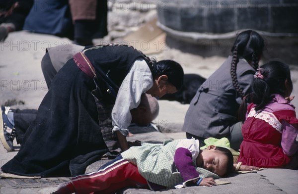 TIBET, Lhasa, Pilgrims at Jokhang Monastery.  Kneeling woman and prostrate child on ground in front of temple entrance.