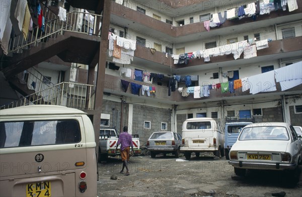 KENYA, Mathare Valley, Nairobi, Middle class housing close to slum area with washing hanging from balconies of four storey buildings and parked cars and person in courtyard in foreground.