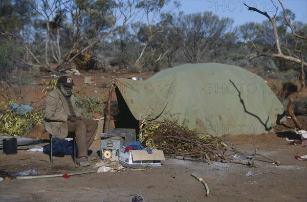 AUSTRALIA, Southern , Oak Valley, Aboriginal man sat on a chair next to a green tent in an Aborigine camp