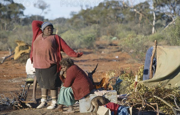 AUSTRALIA, Southern , Oak Valley, Aboriginal women in an Aborigine camp with one women stretching with her arms over her head next to a woman sat on a chair near a small dog and a tent.