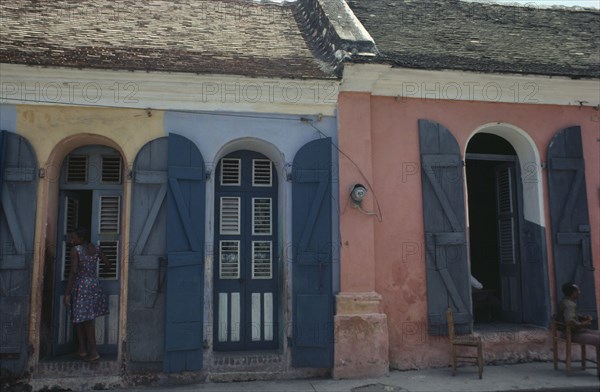 HAITI, Cap Haitien, Street scene with typical colonial style architecture and young woman standing in doorway.