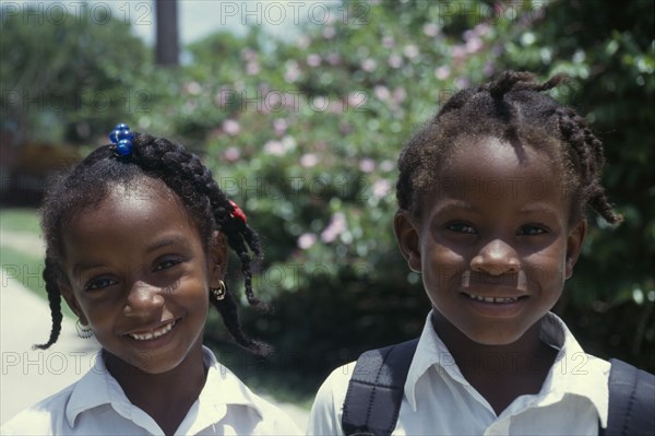 GRENADA, Petit Martinique, Head and shoulders portrait of two smiling schoolgirls with braided hair.