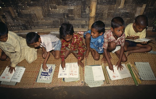 BANGLADESH, Kamalganj, Schoolboys sitting on mats on floor of village school learning to read