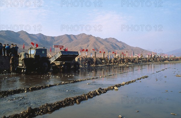 NORTH KOREA, North Hwanghhae Province, Pyongsan County, Juche people in a line reparing flood dykes with red flags fyling and mountains behind them