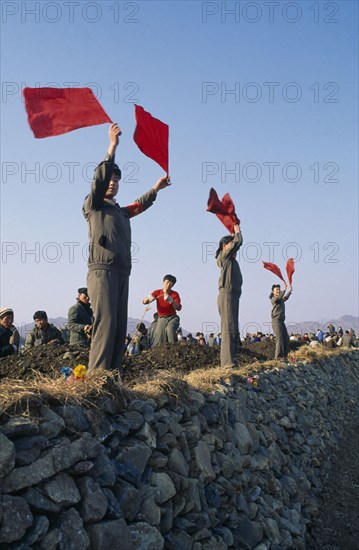 NORTH KOREA, North Hwanghae Province, Pyongsan County, Juche people waving red flags cheering leaders repairing flood damaged dykes.