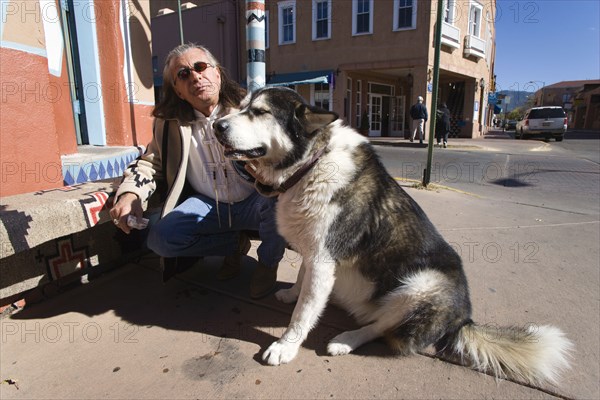 USA, New Mexico, Santa Fe, Native American man feeding his dog outside Father Sky Mother Earth Native American arts and crafts gallery on Water Street