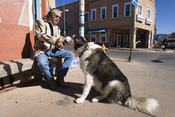 USA, New Mexico, Santa Fe, Native American man feeding his dog outside Father Sky Mother Earth Native American arts and crafts gallery on Water Street