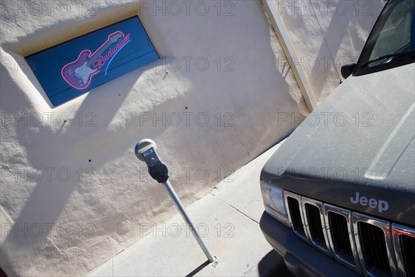 USA, New Mexico, Santa Fe, Illuminated Budweiser sign and electric guitar in window of Blues Club with parking meter and parked jeep in the foreground