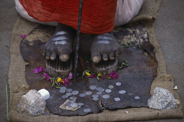 INDIA, Karnataka, Mysore, Cropped shot of sadu standing on nail shoes with coins given by passers-by.