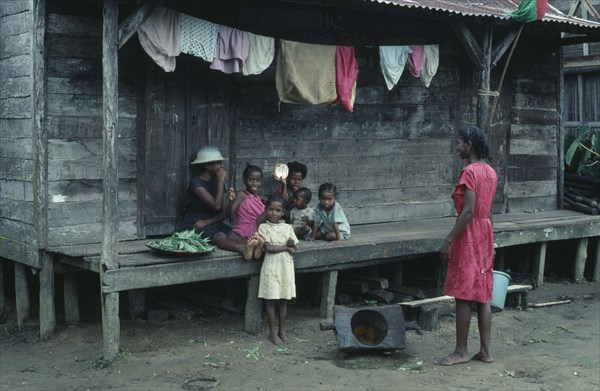 MADAGASCAR, Mananara, Local family sitting on raised wooden veranda of their home with line of washing hanging overhead.