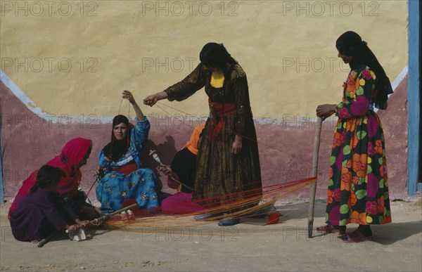 EGYPT, Western Desert, Bedouin, Group of Bedouin women in colourful dress weaving and spinning coloured yarn.