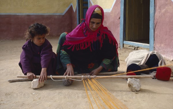 EGYPT, Western Desert, Bedouin, Bedouin woman and child in colourful dress weaving coloured yarn.