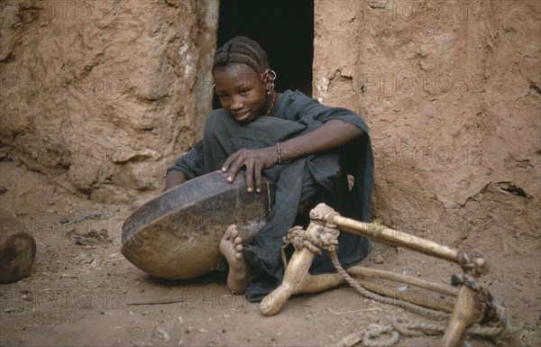 MAURITANIA, Oualata, Young girl cleaning bowl after meal with frame for carrying goods by donkey on her left.