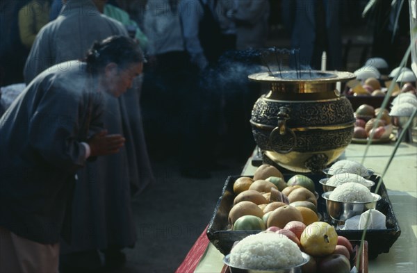 SOUTH KOREA, Religion, Buddhism, Woman praying at an open air altar. Insense burning in a gold urn on table with offerings of fruit and rice bought their by people for Buddhas Birthday