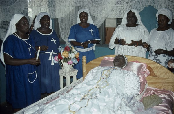 GHANA, South, Teshie, Women surround deceased Ga priestess of the sea god Kanjar laid out on bed during wake.
