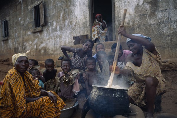 GHANA, Food, Woman in village near Accra stirring cauldron of fufu made from boiled and pounded cassava tubers surrounded by children and other women.