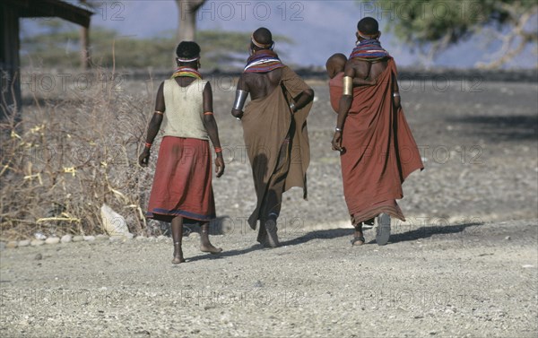 KENYA, People, "El Molo tribeswomen wearing traditional jewellery with one carrying child in sling on her hip, all walking away from camera.  "