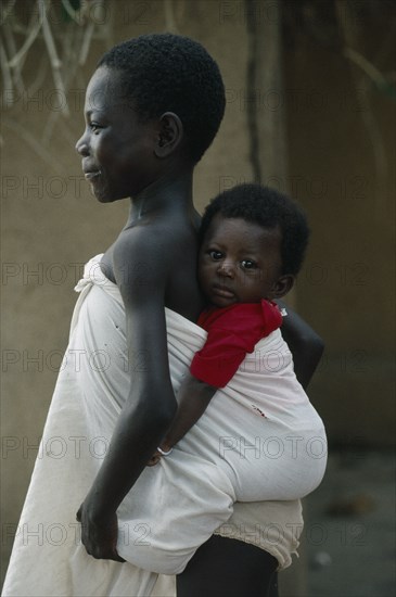 GHANA, Children, Child carrying sibling on her back wrapped in white cotton cloth.