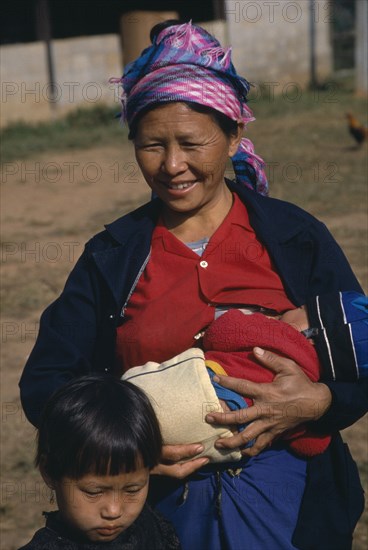 THAILAND, People, Mother breastfeeding baby while standing with older child at her side.