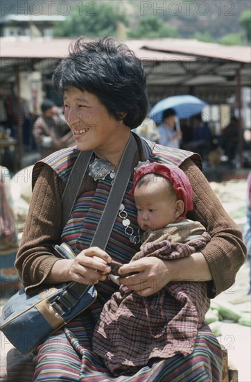 BHUTAN, People, Woman in national dress or kira consisting of rectangular piece of cloth wrapped around body over a blouse or wonju held at the shoulder and waist.  Holding baby on her lap.