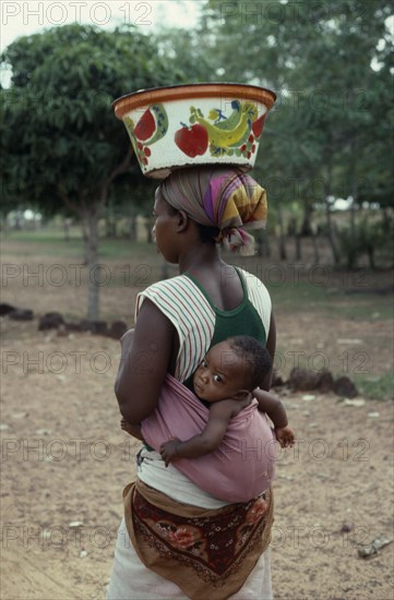 BURKINA FASO, People, Woman carrying baby in sling on her back and painted bowl on her head in area west of Banfora.