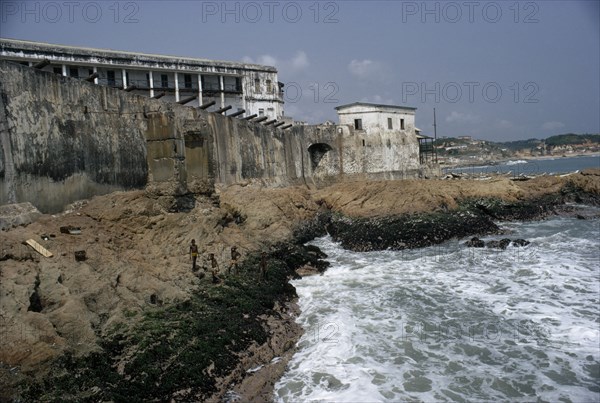 GHANA, Cape Coast, Cape Coast Castle.  Line of cannons along seventeenth century castle ramparts with children playing on rocks below.