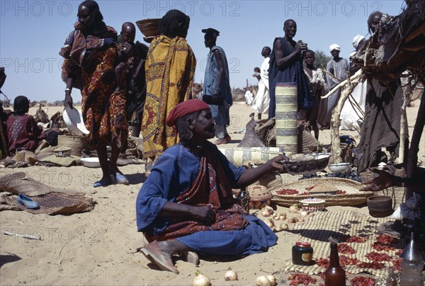 CHAD, Markets, Kanimbo market with woman sat on ground selling foodstuffs with people standing around her