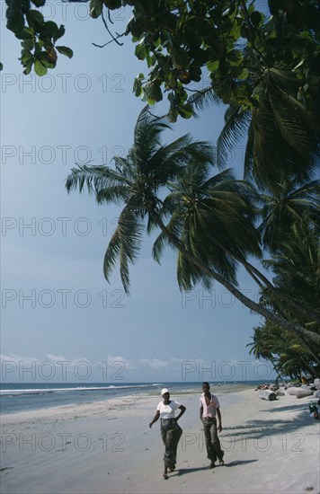 GABON, Landscape, Cape esteries. Man and woman walking along sandy beach lined with overhanging palm trees