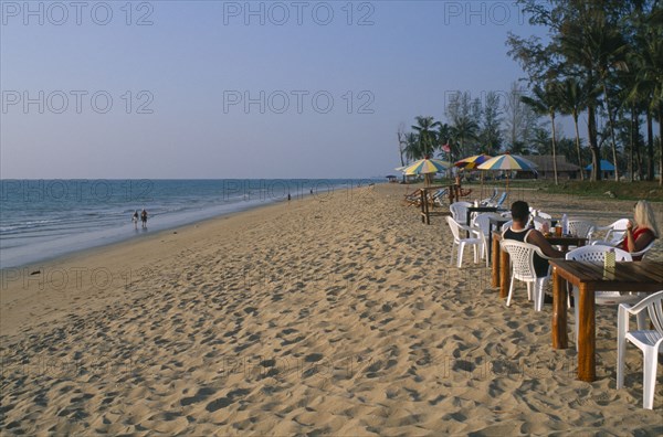 THAILAND, Andaman Sea, Takua Pa district, "Khao Lak, A couple sat at a table on the sandy beach, people walking along the shore and tall palm trees."
