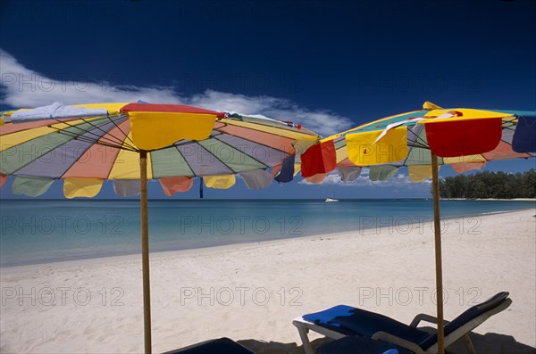 THAILAND, North Phuket, Naiyang Beach, "Two multi coloured parasols and  sun loungers on the sandy beach, boat in the distance."