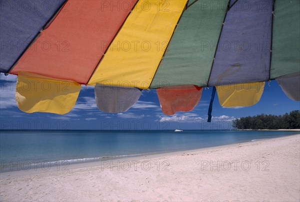 THAILAND, North Phuket, Naiyang Beach, "Close up of a multi coloured parasol on the sandy beach, boat in the distance."